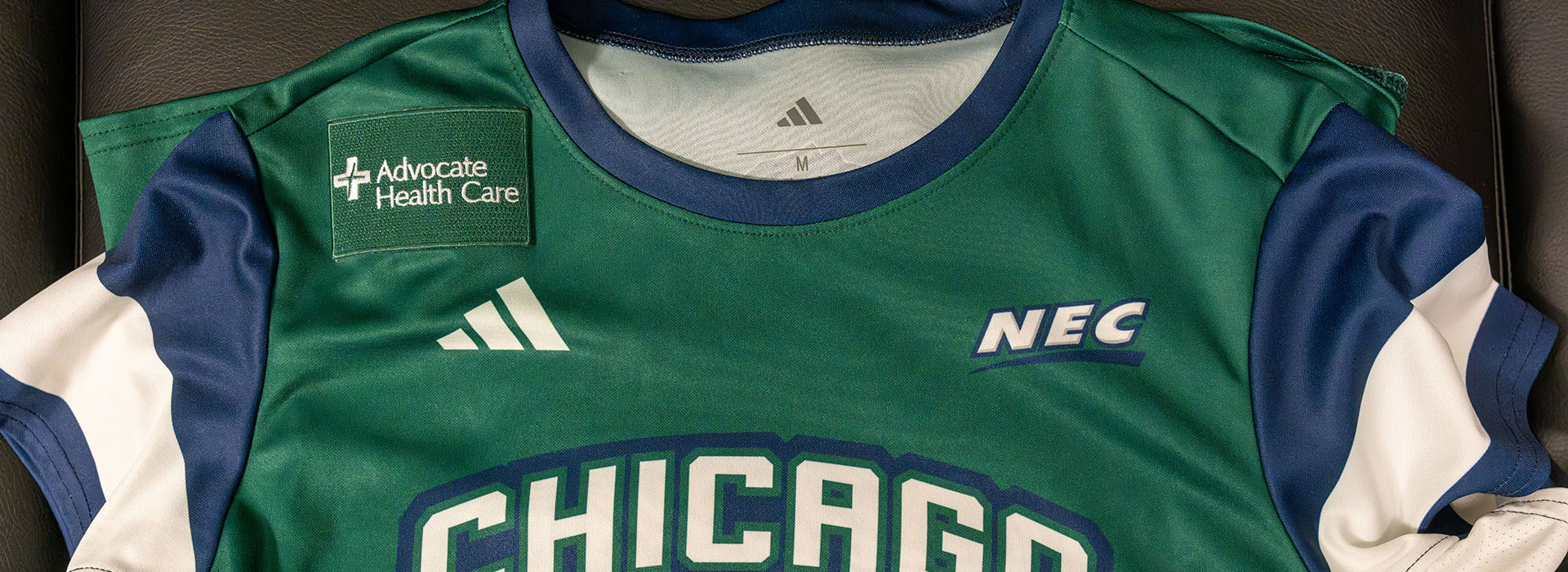 A green, navy blue and white Chicago State University football jersey featuring an Advocate Health Care logo patch, the Adidas logo, and NEC patch.