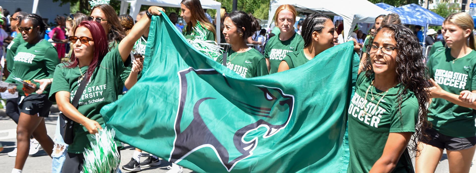 Students in green CSU Shirts, walking in a parade and holding a green banner with cougar logo