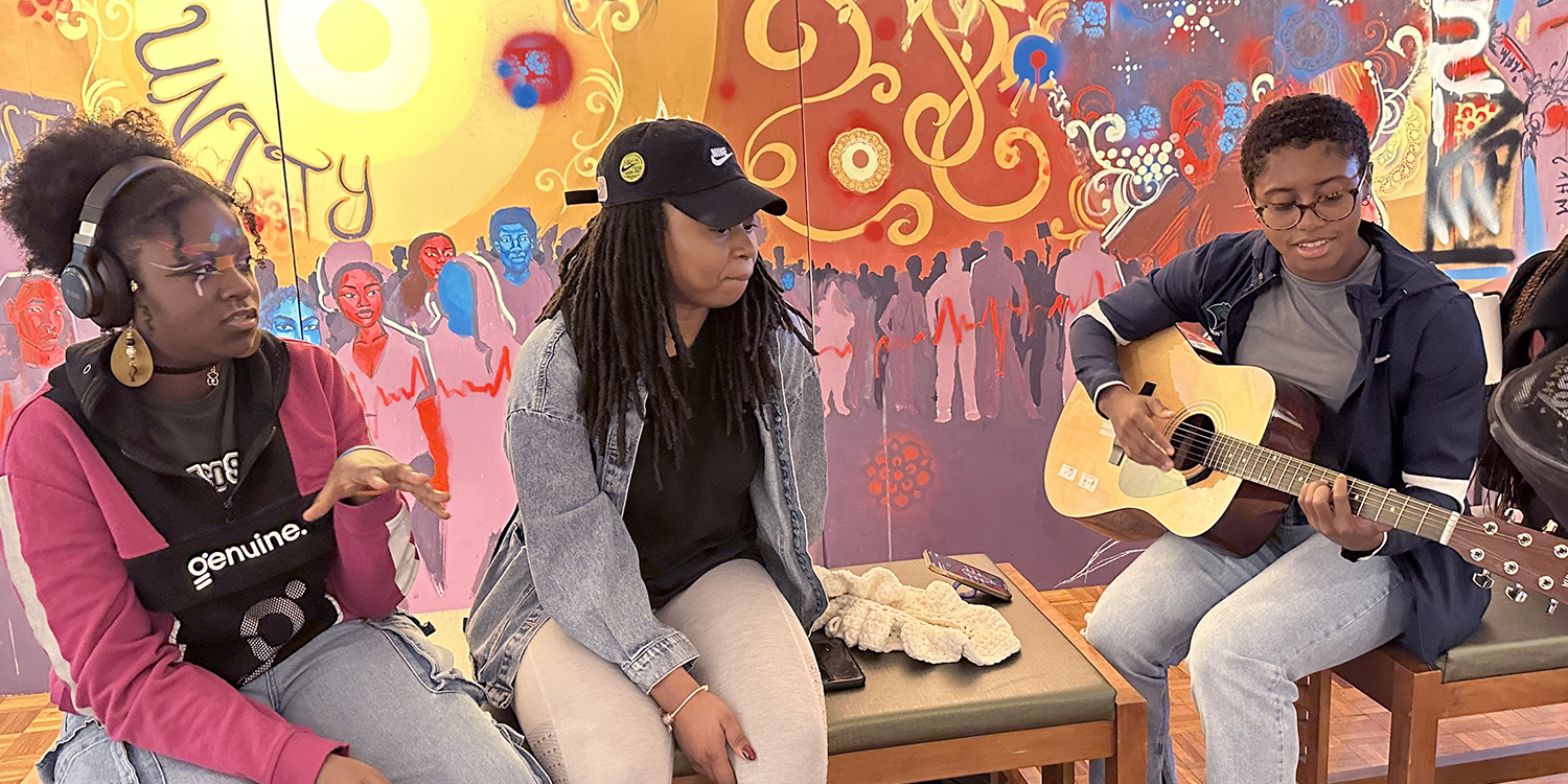 Three students talking and playing guitar in gallery