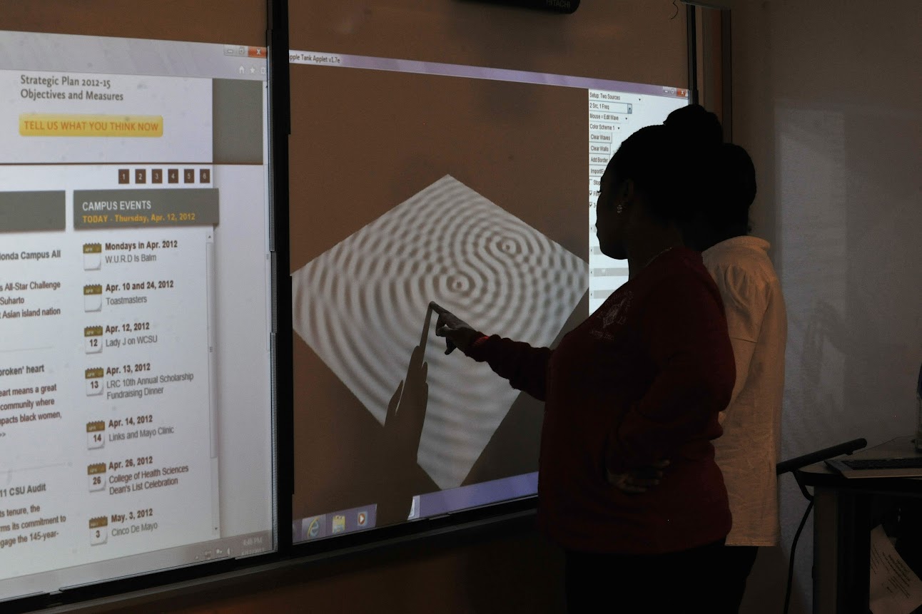 Two students standing in front of a smartboard displaying a ripple tank.