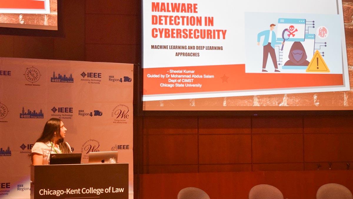 Sheetal Kumar, Chicago State University CIMST student, stands behind a podium while presenting a slide deck on Malware Detection in Cybersecurity.