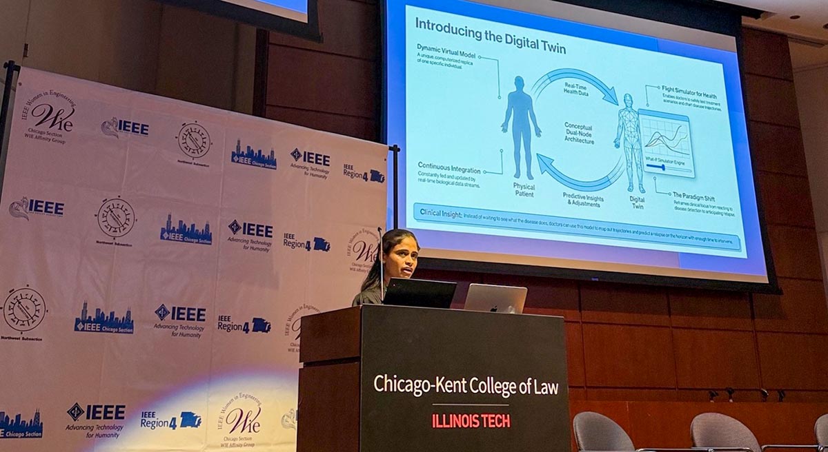 Jyothi Lakshmi Nagaraj, Chicago State University CIMST student, stands at a podium at the Chicago-Kent College of Law, giving a presentation in front of a large screen. The presentation slide is titled 'Introducing the Digital Twin' and features a diagram showing a bidirectional flow of data between a 'Physical Patient' and a 'Digital Twin' (a virtual model), with labels describing it as a 'Flight Simulator for Health.' The background wall behind the speaker features a step-and-repeat of IEEE (Institute of Electrical and Electronics Engineers) and 'Women in Engineering' (WIE) logos.