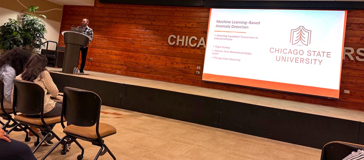 Computer science graduate student Ozgur Gurbuz stands behind a podium and presents his research on  Machine Learning-Based Anomaly Detection.