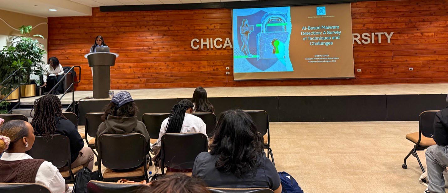 Computer science graduate student Sheetal Kumar presents research from stage with a slide titled "AI-Based Malware Detection: A Survey of Techniques and Challenges," while the audience listens.