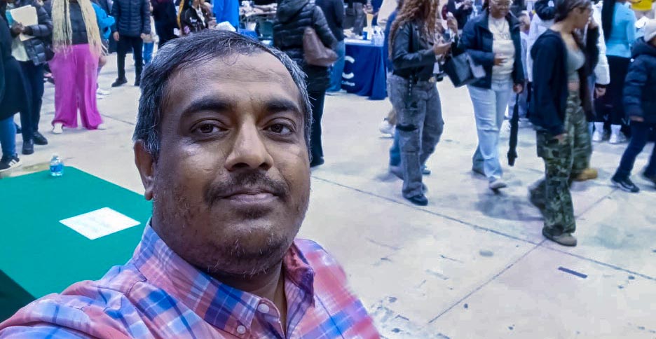 Dr. Saifuddin Saif, professor in the Computing, Information, Mathematical Sciences and Technology, takes a selfie with students in the background.