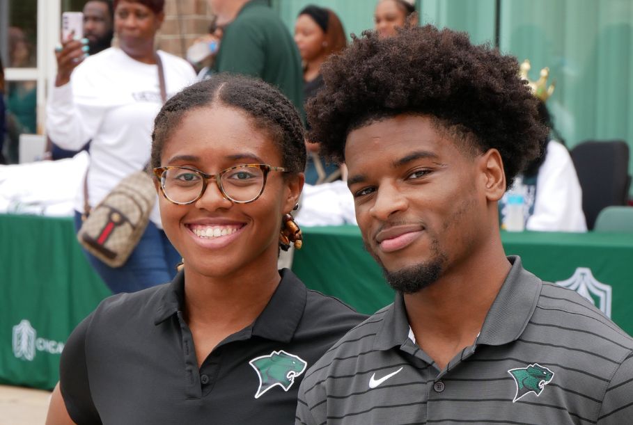 wo students, a man and a woman, smile at the camera during a campus event. Both are wearing polo shirts featuring the Chicago State cougar mascot, and they are styled in casual, professional attire.