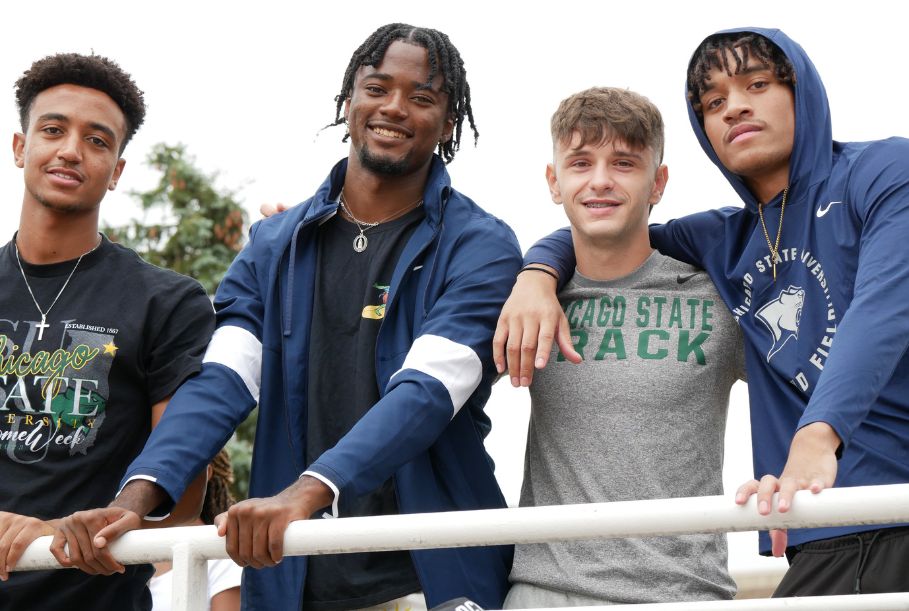 Four Chicago State Track and Field athletes pose together in team-branded gear and smile at an outside event.