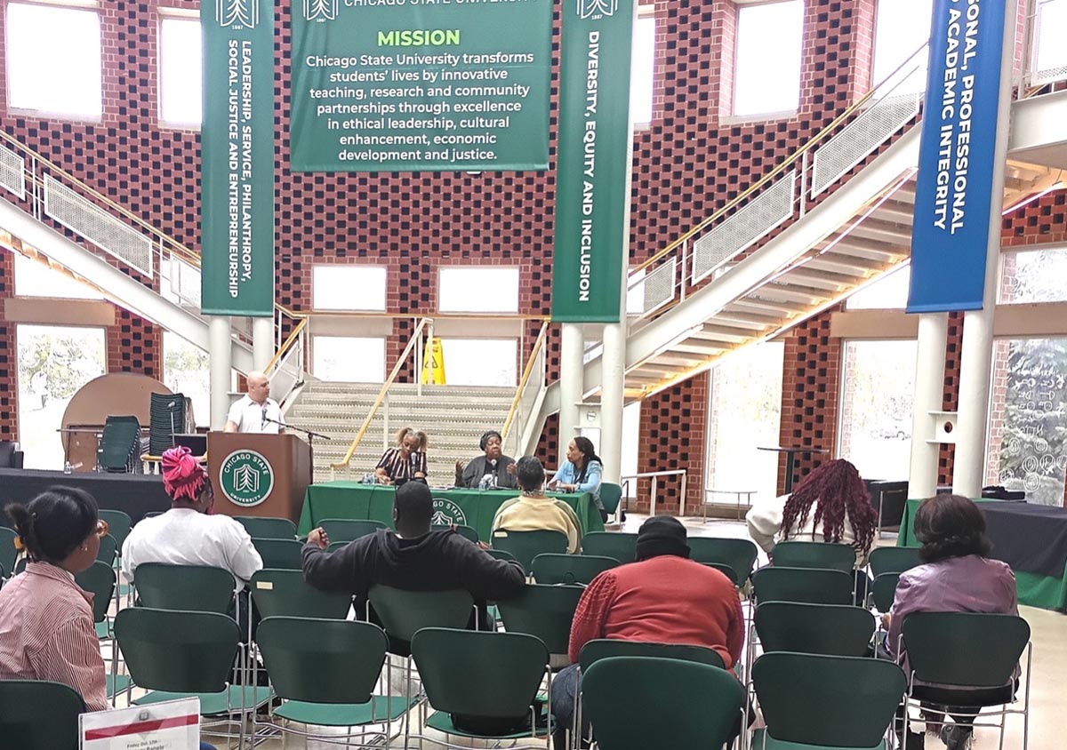 An information session at Chicago State University held in the student union building. A speaker stands at a podium near three seated panelists, positioned beneath large banners displaying the university's mission and values.