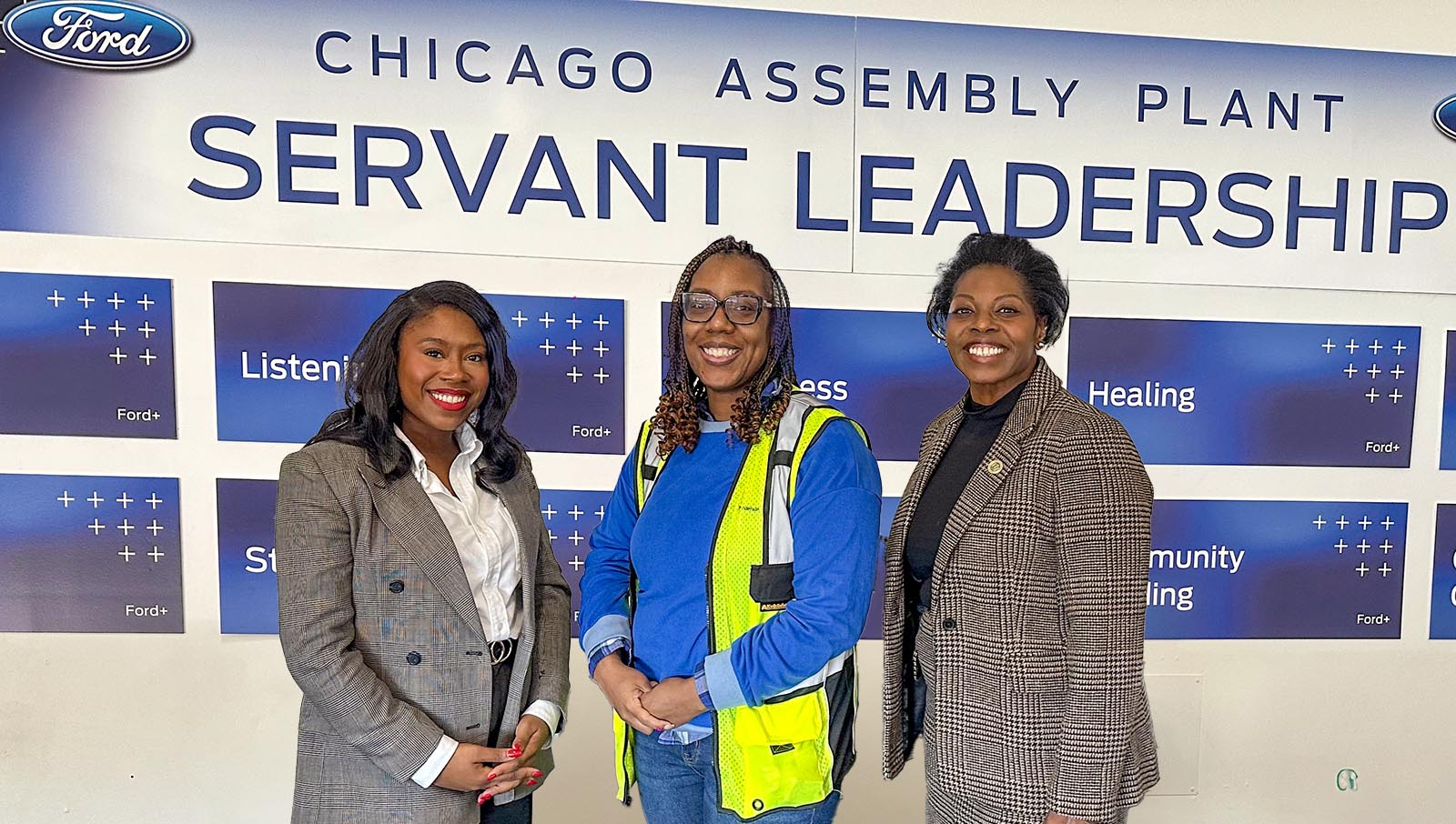 Three women standing in front of a Ford Chicago Assembly Plant sign detailing "Servant Leadership" principles
