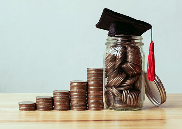 Piles of coins getting larger with grad hat on tallest.