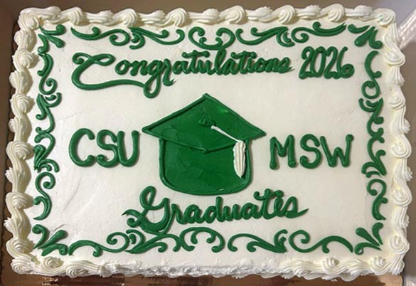 Top-view photo of a white cake with decorative icing around the border. On the cake, icing says "Congratulations 2026 CSU MSW Graduates" with a graduation cap made of green icing and more green decorative icing around the border.